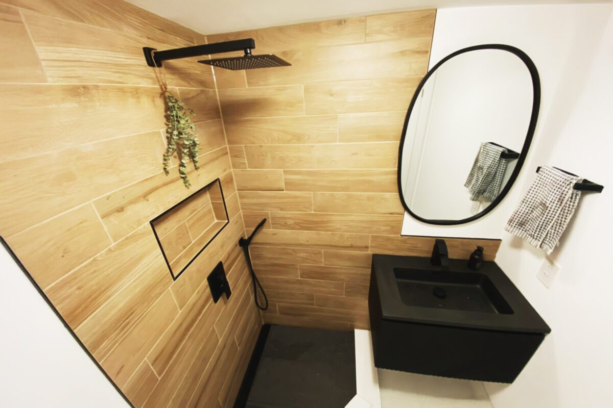 A shower in a bathroom, with brown wood style custom tile and black finishings.