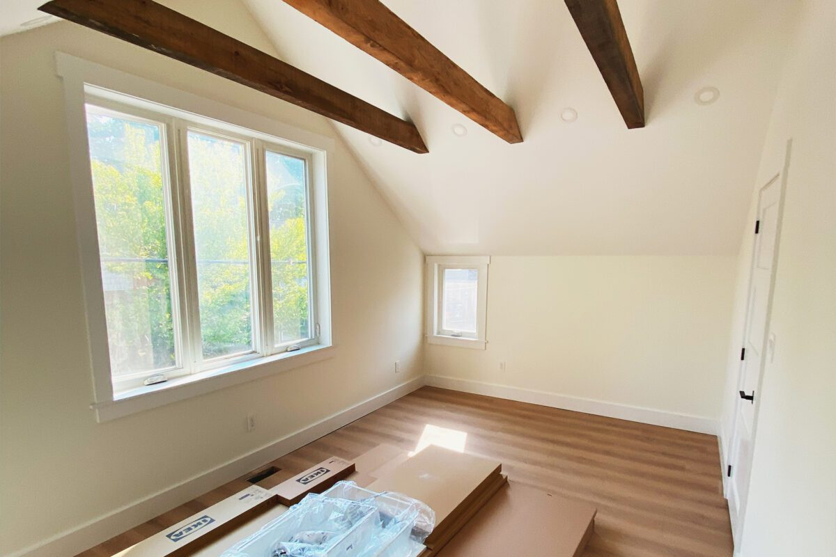 An open bedroom with a large window, wood floors and exposed trusses.
