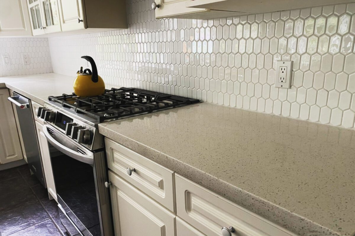 Look down a countertop at a gas stove in front of a newly installed backsplash with an old-fashioned kettle on it.