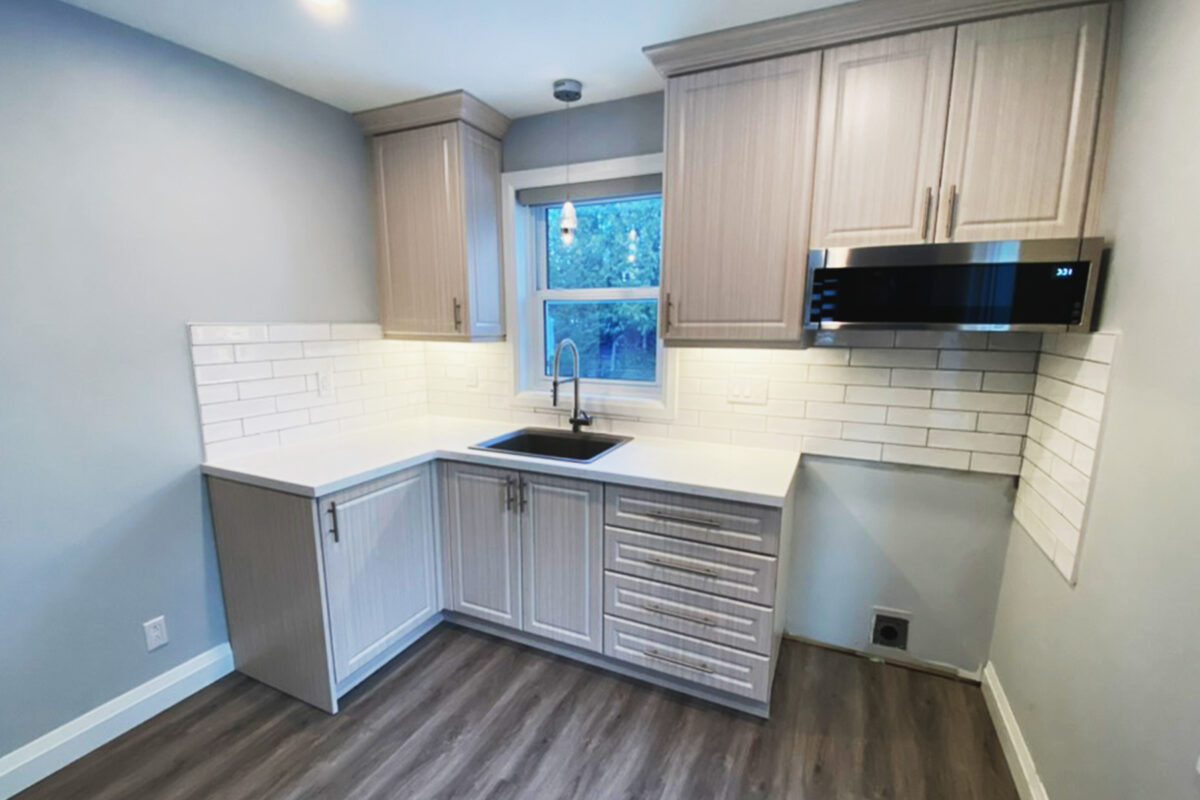 A kitchen with a tile backsplash and black finishings on a new vinyl floor.